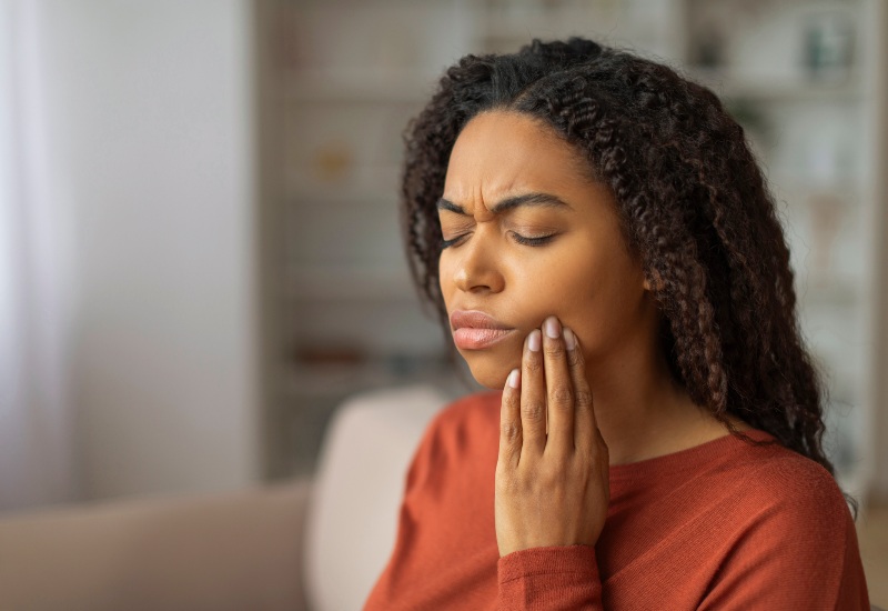 A woman holding her jaw in pain emphasizes the need for emergency dental treatment in Warrenville