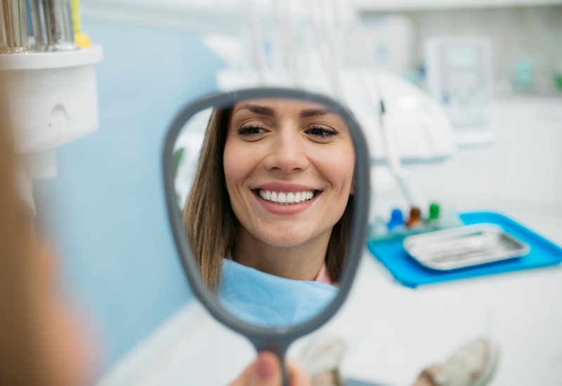 A woman admiring her bright, white smile in a mirror after a smile makeover in Warrenville, IL
