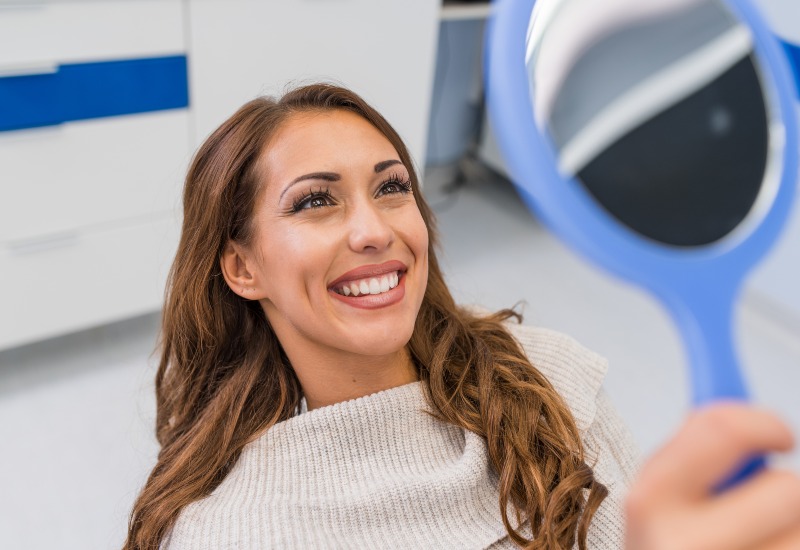Woman smiles seeing the post-whitening results in mirror at dental office in Warrenville, IL