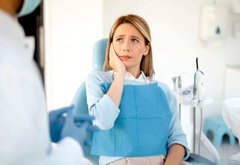 Patient with tooth sensitivity holds sore jaw while speaking with dentist in Warrenville, IL